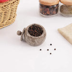 Oceanic marble salt cellar filled with black peppercorns, lid resting beside it, 3 inches wide and tall