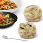 Two 4 inch green onyx marble salt cellars with lids and a stainless steel spoon beside plated noodle dishes