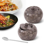 Two 4 inch oceanic marble salt cellars with lids and a stainless steel spoon beside plated noodle dishes