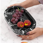 Hands holding a black footed marble bowl with grapes and a peach