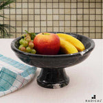 Black marble footed fruit bowl on a pedestal base holding an apple, bananas and grapes