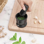 Hand grinding fresh green herbs into a paste with a black marble mortar and pestle, beside garlic, ginger and mint