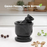 Black marble mortar and pestle on a kitchen counter with whole peppercorns, cardamom pods and fresh coriander