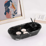Black oval marble tray holding tealights and a reed diffuser beside books