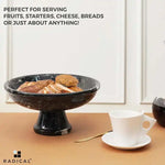 Black marble pedestal bowl raised on a stem holding sliced bread and rolls beside a coffee cup