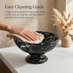 Black marble pedestal fruit bowl being wiped clean with a cloth on a countertop