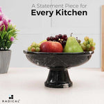 Black marble pedestal fruit bowl on a footed stem holding apples, grapes and a pear on a kitchen counter