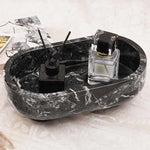 Black oval marble trinket dish holding a reed diffuser and perfume beside books