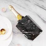 Black marble hexagon wine chiller lying beside a champagne bottle on marble