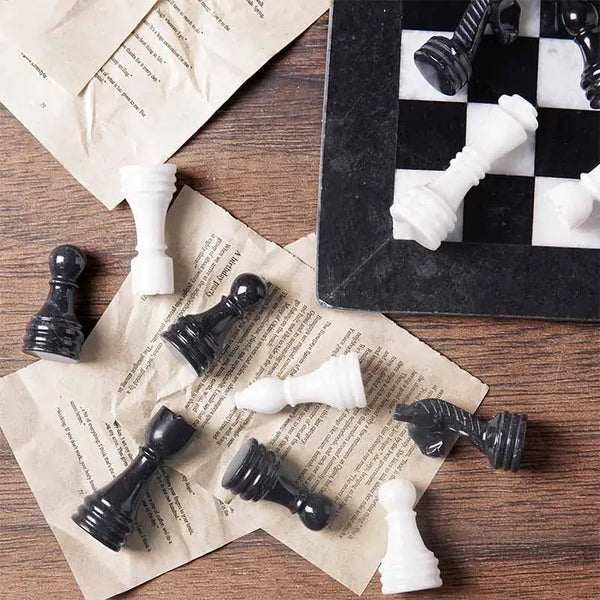 Black marble and white chess pieces scattered on book pages — board corner detail by RADICALn