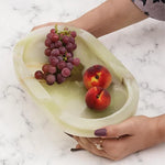 Hands holding a green onyx footed marble bowl with grapes and a peach