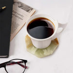Green onyx octagon marble coaster under a white coffee cup beside a newspaper and glasses