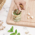 Hand grinding fresh green herbs into a paste with a green onyx marble mortar and pestle, beside garlic, ginger and mint