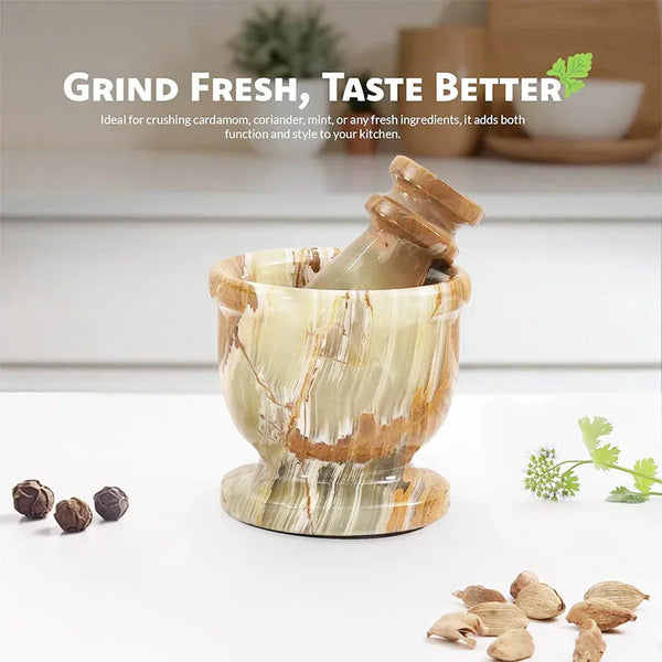 Green onyx marble mortar and pestle on a kitchen counter with whole peppercorns, cardamom pods and fresh coriander