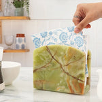 Hand pulling a floral napkin from a green onyx marble napkin holder in a kitchen