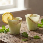Pair of green onyx marble shot glasses garnished with lemon and mint on wood
