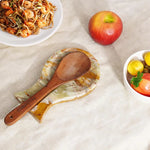 Green onyx marble utensil rest holding a wooden spoon beside a plate of noodles