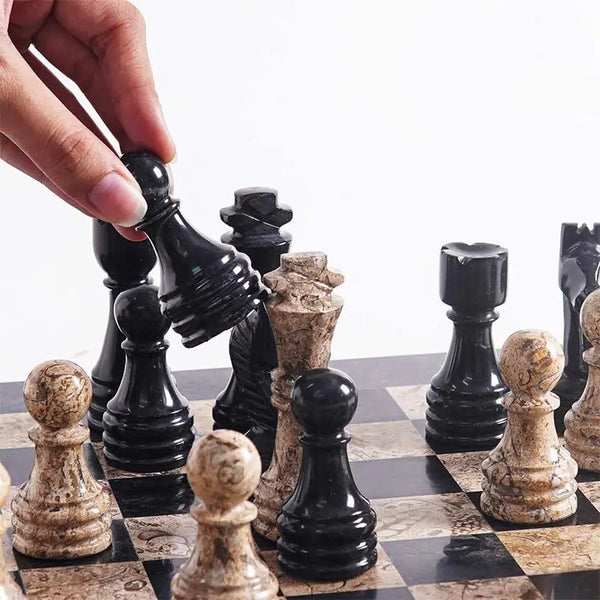 Hand lifting black marble bishop piece — black and fossil coral chess pieces in starting position by RADICALn