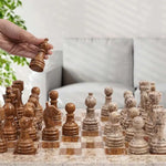 Hand lifting dark brown marble rook piece — fossil coral and dark brown marble chess set 15 inch in home living room by RADICALn