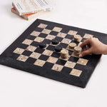 Hand placing fossil coral marble checkers disc mid-game — black and fossil coral marble checkers set 15 inch with books by RADICALn