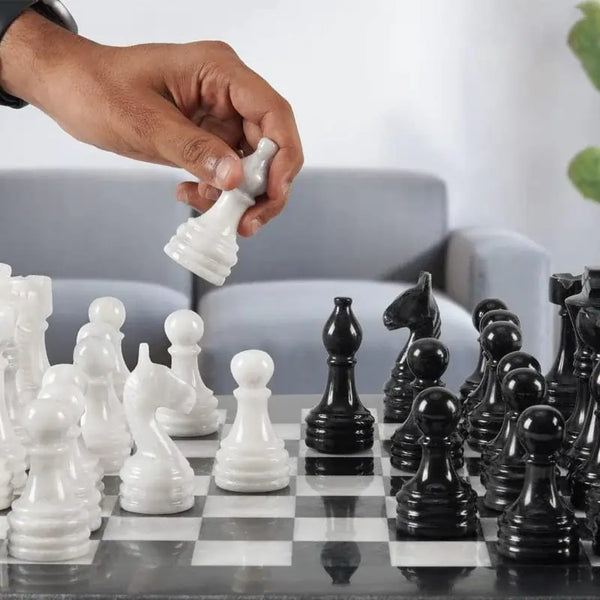 Hand placing white marble queen piece on black and white natural marble chess board — RADICALn 15-inch set
