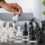 Hand placing white marble queen piece on black and white natural marble chess board — RADICALn 15-inch set