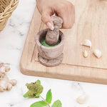 Hand grinding fresh green herbs into a paste with a marinara marble mortar and pestle, beside garlic, ginger and mint