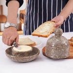 Butter being spread on toast with the marble knife from a oceanic marble butter dish, dome lid resting on a wooden board