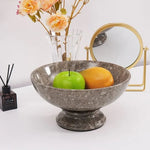 Oceanic marble pedestal fruit bowl holding a green apple and persimmon on a console table beside a vase and mirror