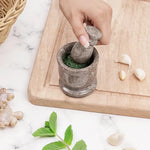 Hand grinding fresh green herbs into a paste with an oceanic marble mortar and pestle, beside garlic, ginger and mint