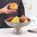Hand placing an apple into a oceanic marble pedestal fruit bowl already holding a pear and plums