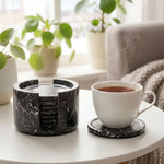 Round black marble coaster set and holder on a coffee table with a cup of tea