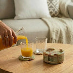Round green onyx marble coaster set with holder on a coffee table under glasses of orange juice