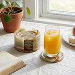 Round green onyx marble coaster set with holder beside a glass of orange juice on a linen cloth