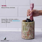 Hand placing a sparkling bottle into a round green onyx marble wine chiller on a kitchen counter