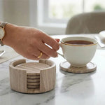 Hand lifting a tea cup from a round natural brown marble coaster beside its matching stone holder
