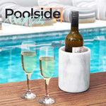 Round white marble wine cooler chilling a bottle beside two champagne flutes poolside