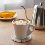 Round white onyx marble coaster with red veining under a latte cup on a wooden kitchen table