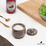 Small oceanic marble seasoning keeper filled with salt, stainless steel knob lid set to the side on a countertop