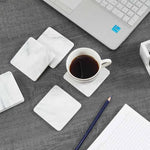 Square white marble coasters on a white desk with a laptop, notepad and cup of coffee