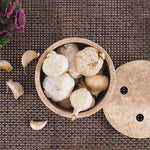 Overhead view of a travertine marble garlic keeper full of garlic bulbs, vented lid resting alongside