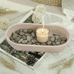 Travertine oval marble tray holding a candle and river pebbles on a styled coffee table