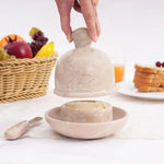 Hand lifting the dome lid off a verona marble butter dish set on a breakfast table with fruit and toast