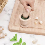 Hand grinding fresh green herbs into a paste with a verona marble mortar and pestle, beside garlic, ginger and mint