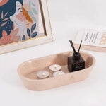 Verona oval marble tray holding tealights and a reed diffuser beside books