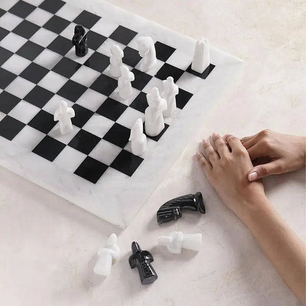 White and black antique marble chess set in play — medieval figurative pieces mid-game with hands beside board by RADICALn