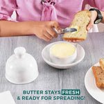 Butter being spread on toast with the marble knife from a white marble butter dish, dome lid resting on a wooden board