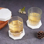 White octagon marble coasters under two whiskey glasses on a white table
