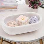 White footed marble trinket bowl holding a candle and rattan balls on a coffee table