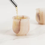 Drink being poured into a white onyx marble shot glass on a marble surface